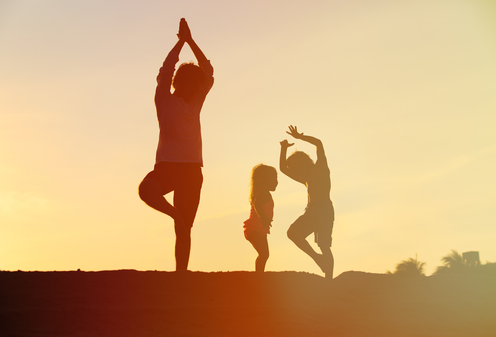father with kids silhouettes doing yoga at sunset